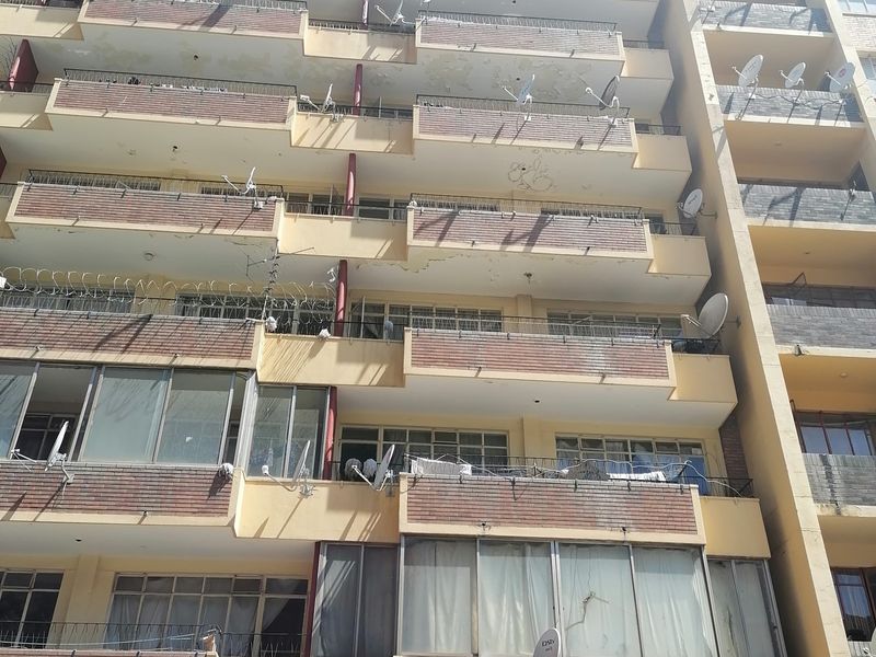 Exterior view of a multi-story apartment building featuring brick facade, multiple balconies, and security fencing.