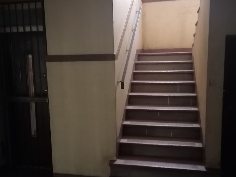 A dimly lit interior hallway featuring a staircase with a metal handrail and a security gate entrance.