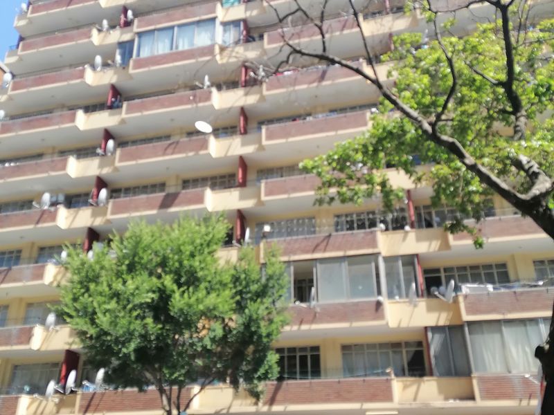 Front elevation of a multi-story apartment building featuring multiple balconies, brick detailing, and ground-level secure parking access.