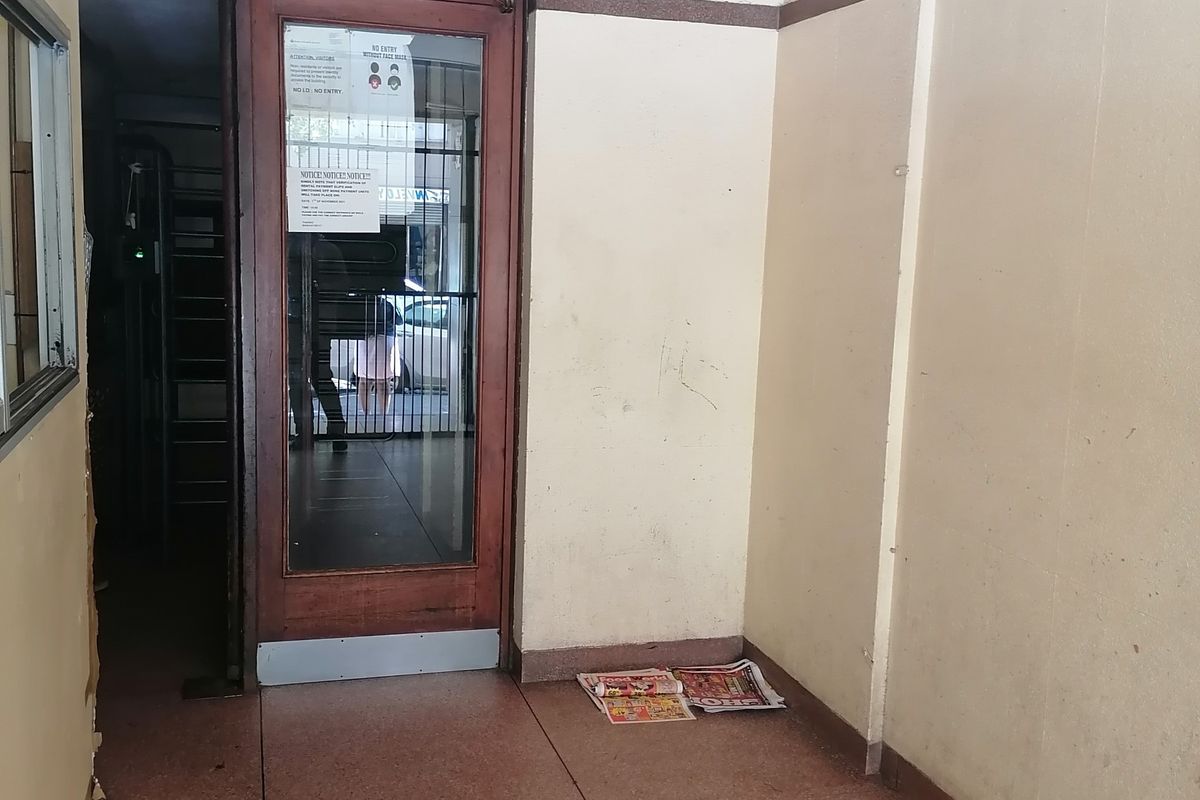 A simple building entrance area featuring terrazzo flooring and a timber-framed glass door, currently in need of cosmetic refurbishment.