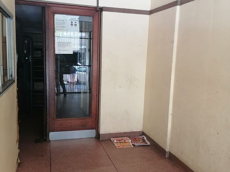 A simple building entrance area featuring terrazzo flooring and a timber-framed glass door, currently in need of cosmetic refurbishment.