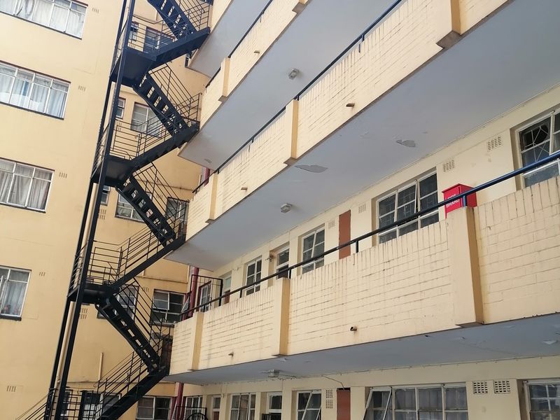 Exterior view of a multi-story apartment building featuring a prominent external steel fire escape staircase and brick facade with balcony access.