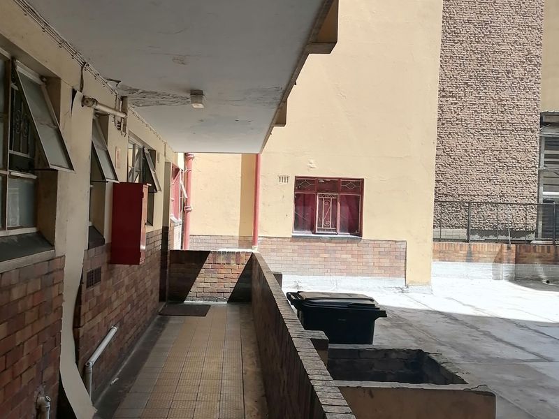 An exterior rear walkway area featuring brick walls and tiled flooring, showing signs of wear and maintenance requirements.