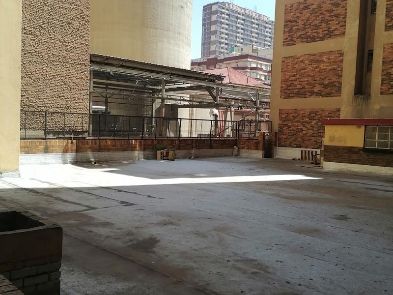 An open-air concrete balcony or terrace area featuring brick perimeter walls and metal railings, situated between adjacent building structures.