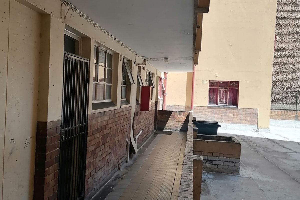 Exterior rear walkway of the flat featuring brick facade, tiled flooring, and security gate access to the unit.