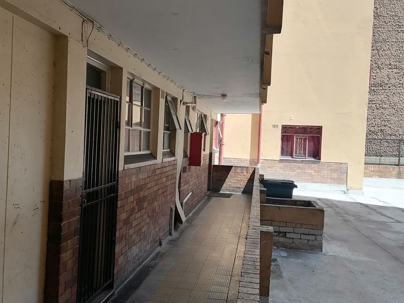 Exterior rear walkway of the flat featuring brick facade, tiled flooring, and security gate access to the unit.