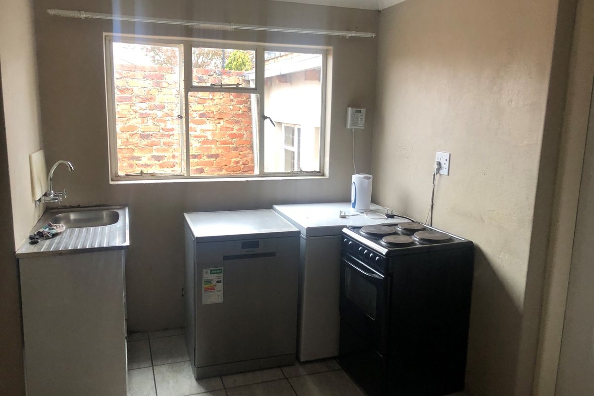 A functional kitchen area featuring a stainless steel sink, tiled flooring, and space for freestanding appliances under a window.