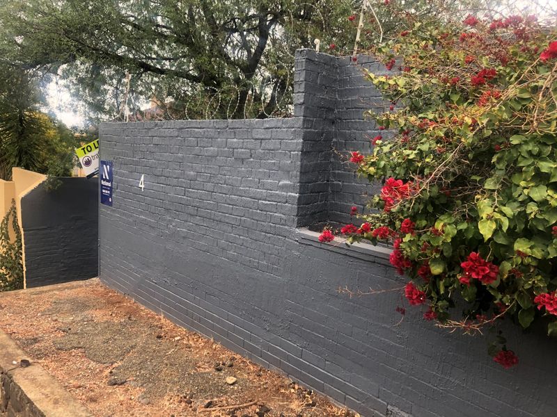A painted brick boundary wall featuring security razor wire and house number signage, providing a secure perimeter for the property.