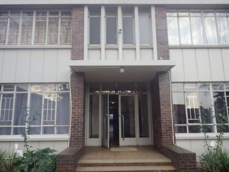 Front entrance of a multi-story flat building featuring brick masonry, metal-framed windows, and a tiled entryway.