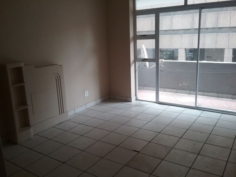 An empty living room featuring tiled flooring, a built-in shelving unit, and a large sliding glass door providing access to an outdoor balcony area.