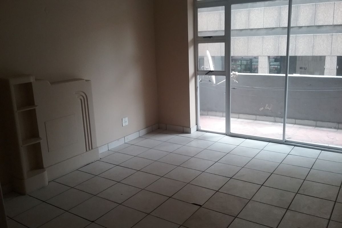 An empty living room featuring tiled flooring, a built-in shelving unit, and a large sliding glass door providing access to an outdoor balcony area.