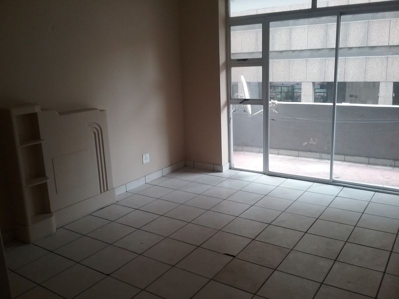 An empty living area featuring tiled flooring, a built-in shelving unit, and a large sliding glass door providing access to an exterior balcony.