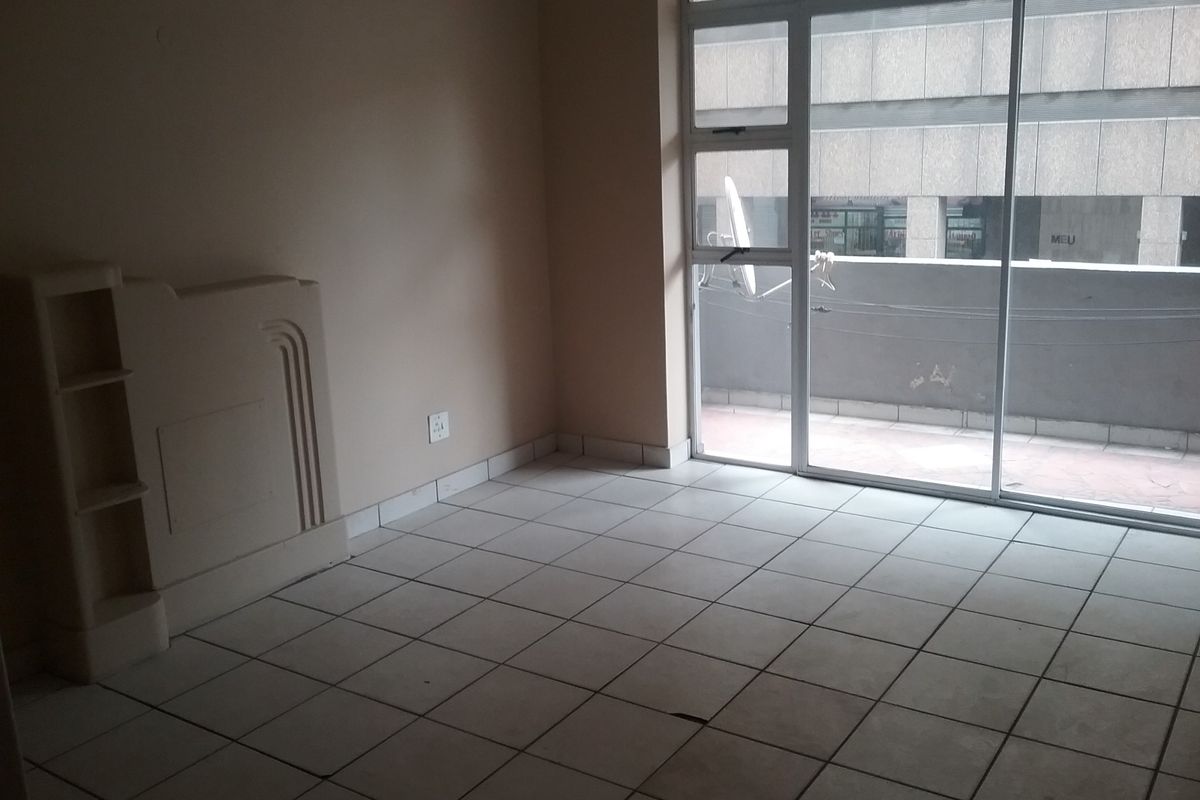 An empty living area featuring tiled flooring, a built-in shelving unit, and a large sliding glass door providing access to an exterior balcony.