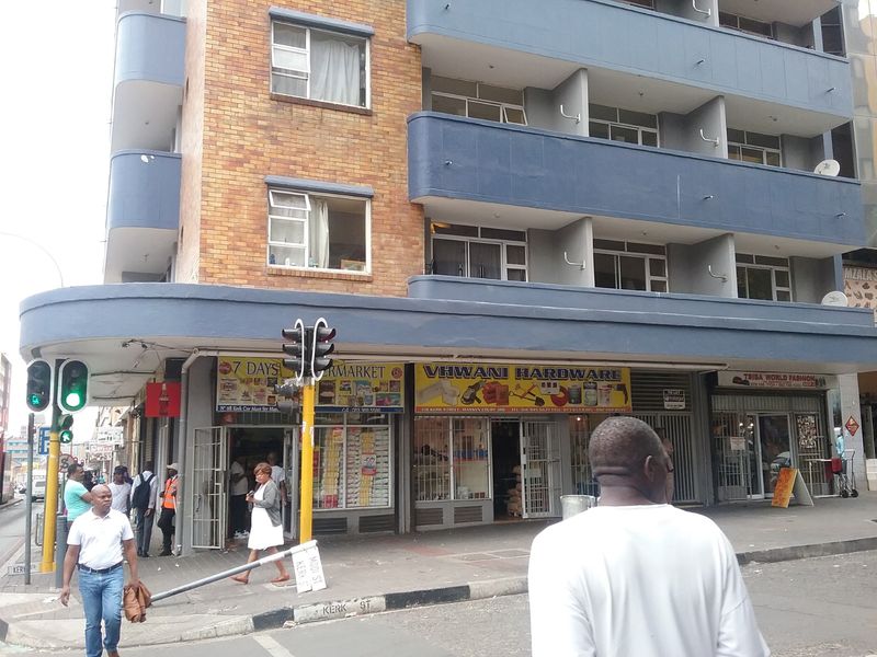 Street-level view of a multi-story commercial building featuring ground floor retail storefronts and residential units with balconies above.