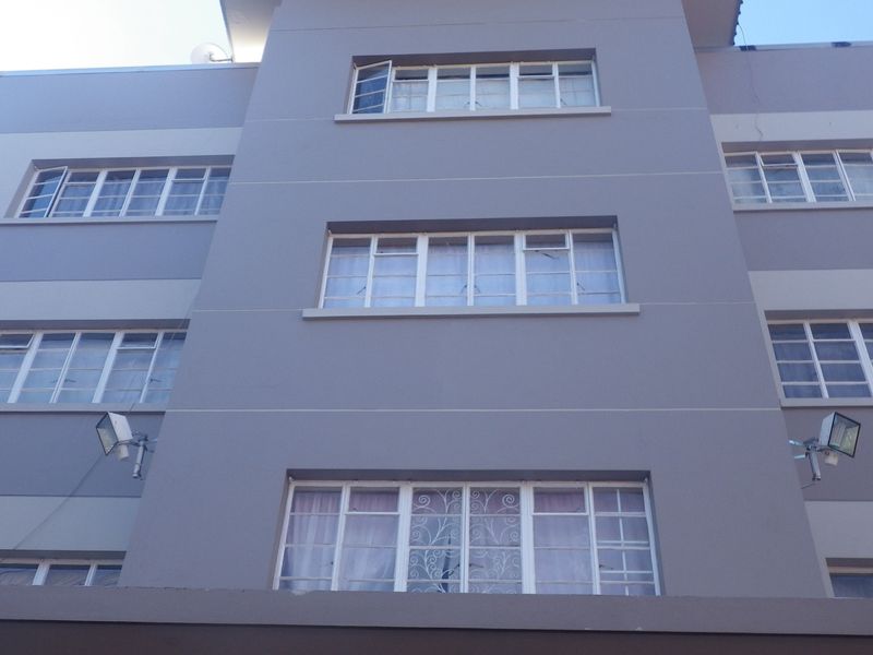 A low-angle view of a multi-story apartment building facade featuring grey painted exterior walls and multiple steel-framed windows with security bars.