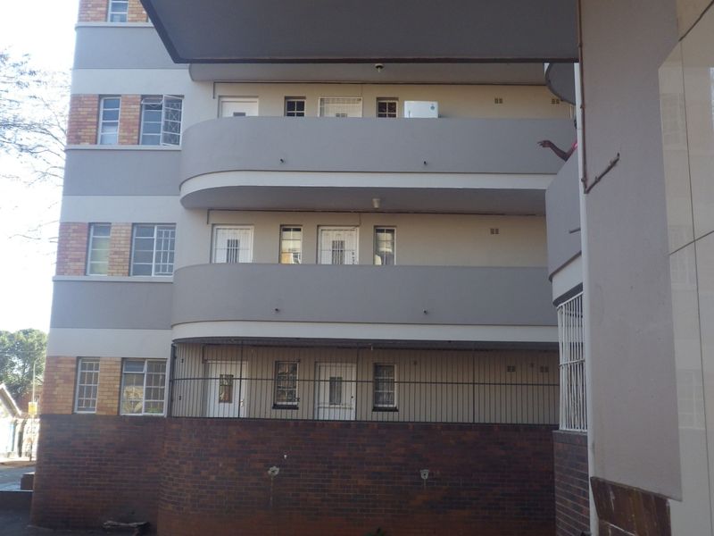 A view of the rear elevation of a multi-story flat building featuring brick and rendered finishes with multiple balconies and security features.