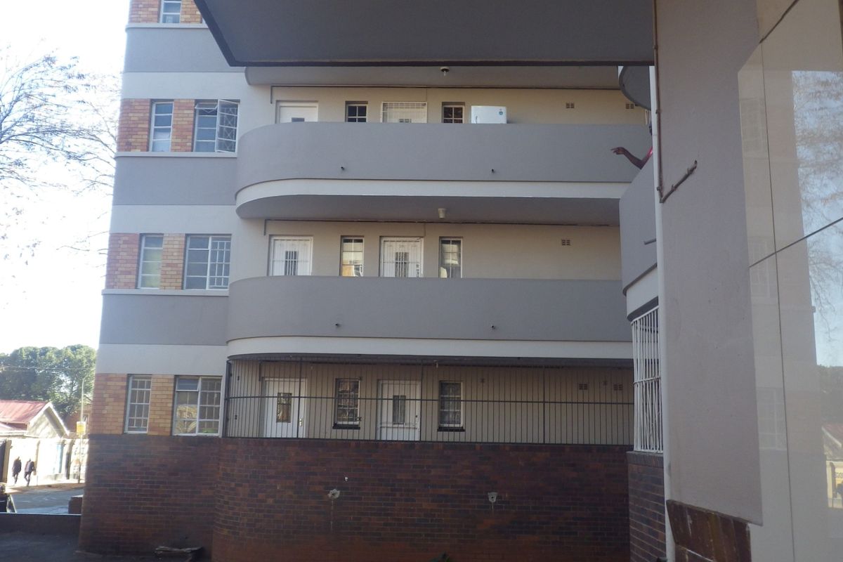 A view of the rear elevation of a multi-story flat building featuring brick and rendered finishes with multiple balconies and security features.