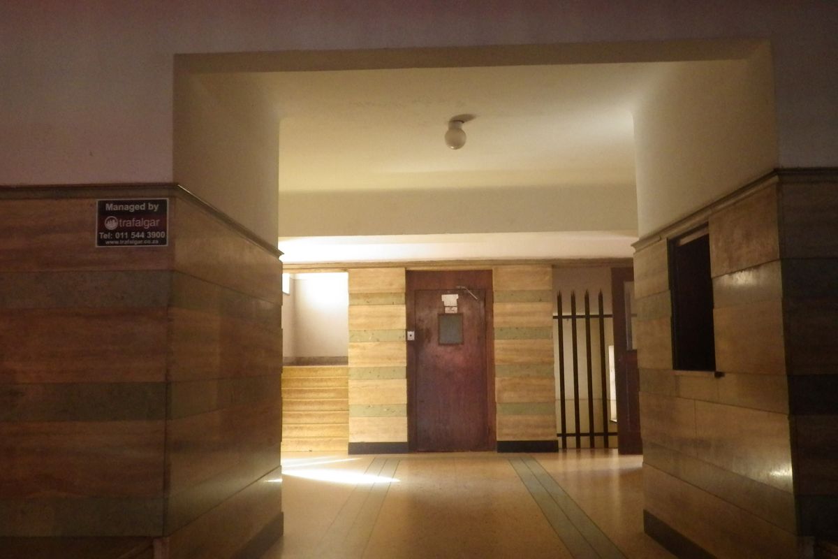 A spacious apartment building hallway featuring wood paneling, tiled flooring, and a secure entrance door.