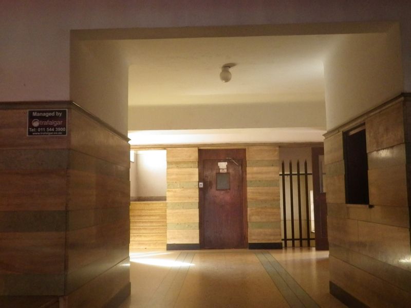 A spacious apartment building hallway featuring wood paneling, tiled flooring, and a secure entrance door.