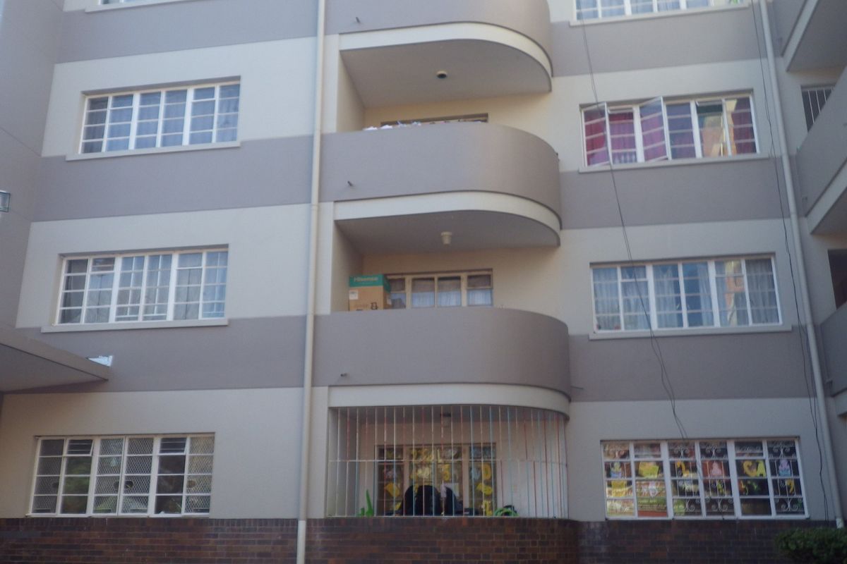 Exterior view of a multi-story apartment building featuring curved balconies, brick base detailing, and security bars on lower-level windows.