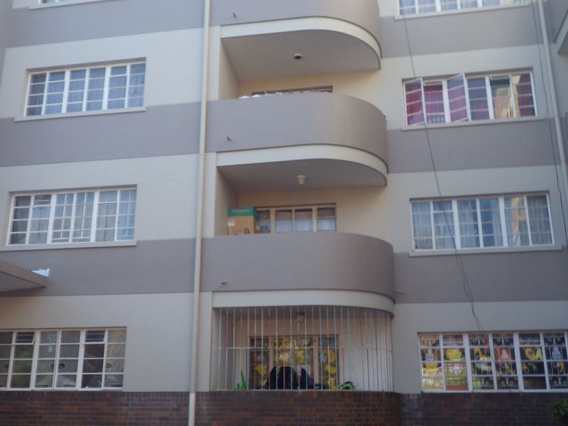 Exterior view of a multi-story apartment building featuring curved balconies, brick base detailing, and security bars on lower-level windows.
