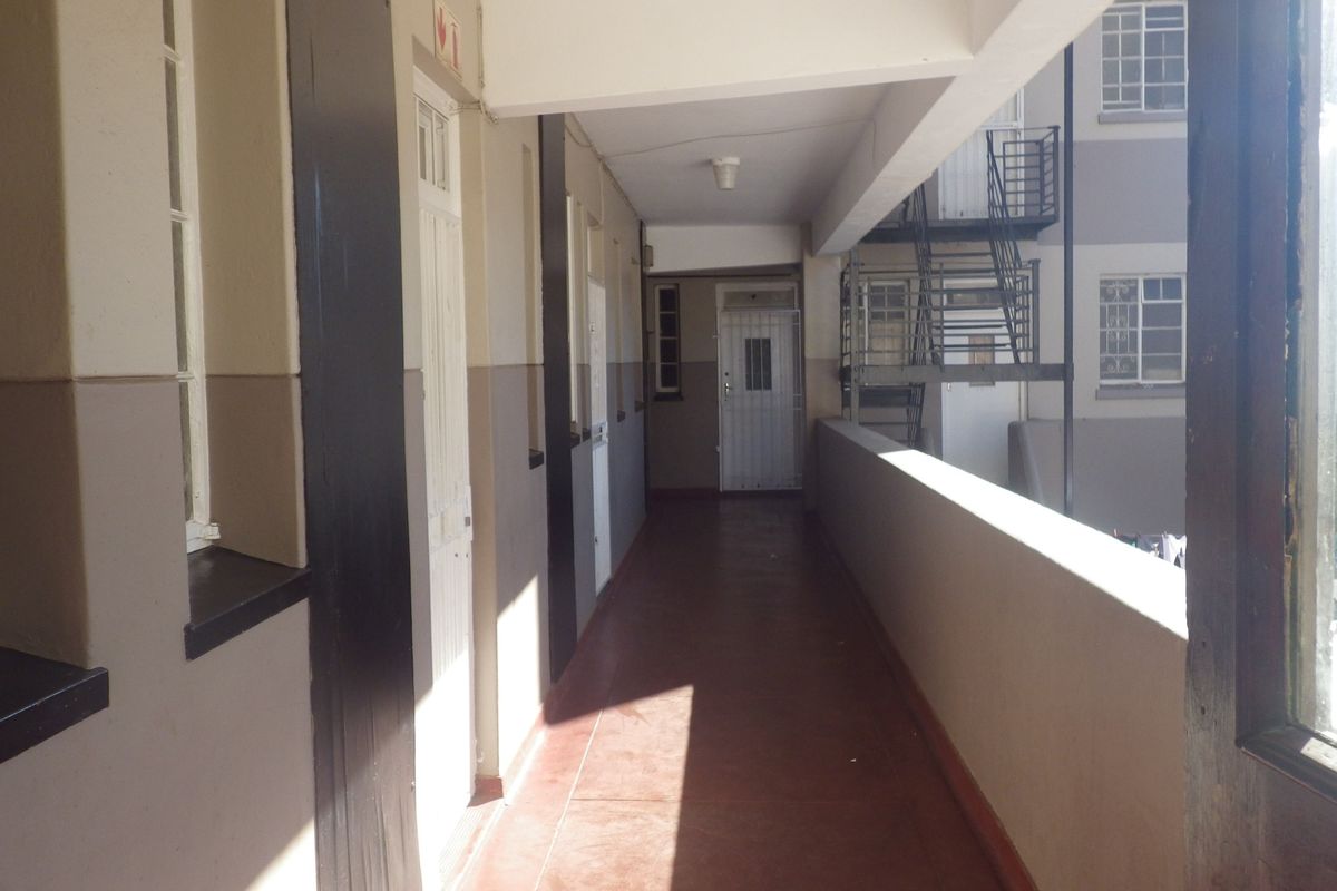 An exterior communal hallway or walkway featuring concrete balustrades, security gates, and access to an external staircase in a flat complex.