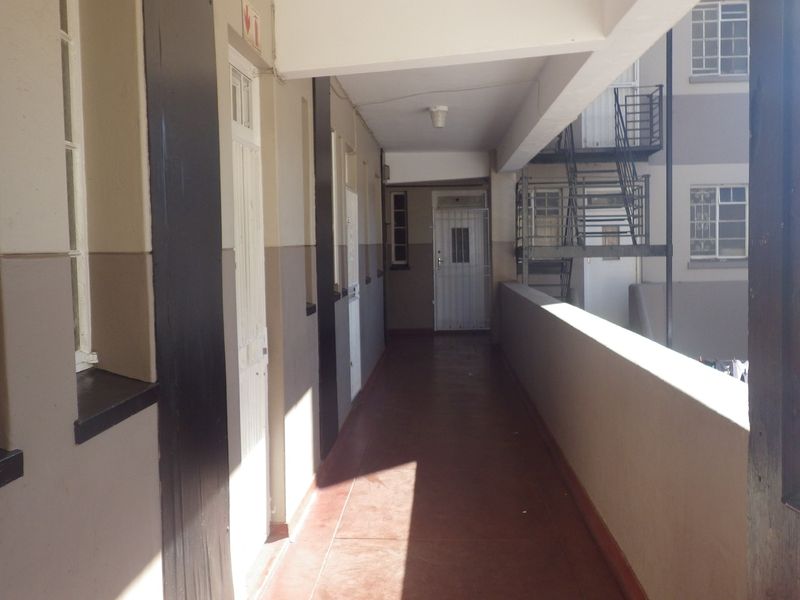 An exterior communal hallway or walkway featuring concrete balustrades, security gates, and access to an external staircase in a flat complex.