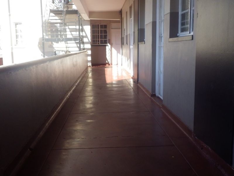An exterior communal walkway providing access to apartment units, featuring a concrete floor and metal security gate.