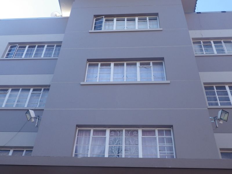 A view of the multi-story apartment building facade featuring grey painted exterior walls, multi-pane windows, and security bars.
