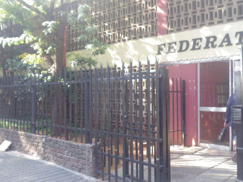 Front exterior view of the building featuring security fencing, a brick boundary wall, and a decorative breeze block screen facade.