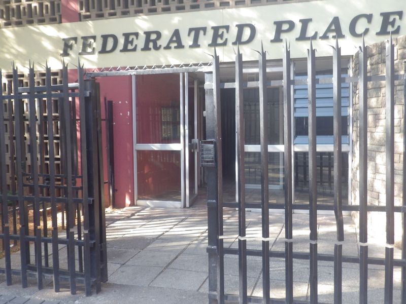 Front entrance of Federated Place featuring a secure gated access point, intercom system, and paved walkway leading to the main building entrance.