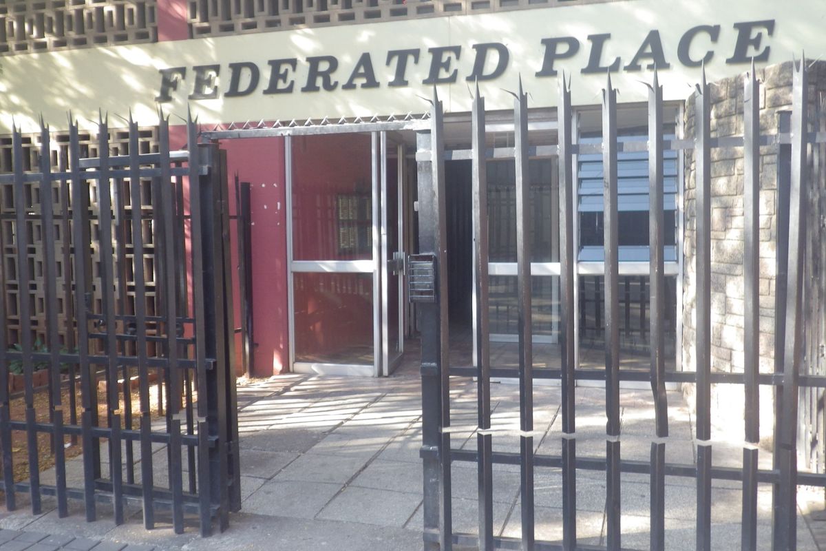 Front entrance of Federated Place featuring a secure gated access point, intercom system, and paved walkway leading to the main building entrance.