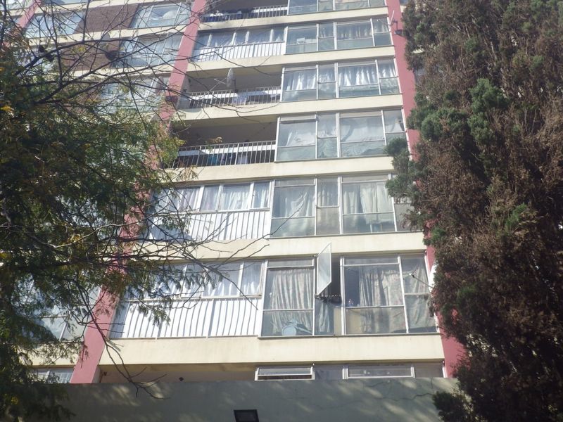Exterior view of a multi-story apartment building featuring balconies and aluminium-framed windows, showing signs of general wear and tear.