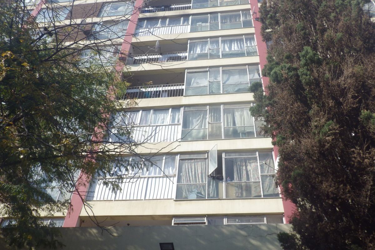 Exterior view of a multi-story apartment building featuring balconies and aluminium-framed windows, showing signs of general wear and tear.