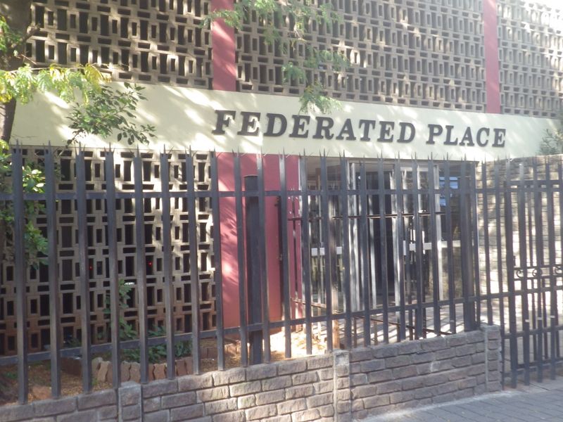 Front facade of Federated Place featuring decorative concrete screen blocks, secure perimeter fencing, and a brick boundary wall.