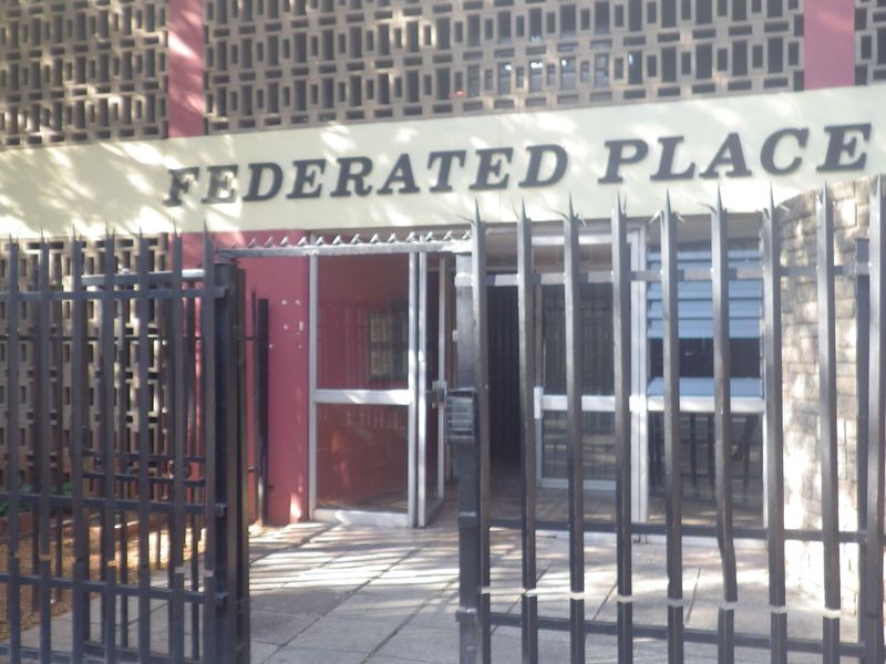 The front entrance of Federated Place featuring a secure gated access point, paved walkway, and decorative breeze block architectural detailing.