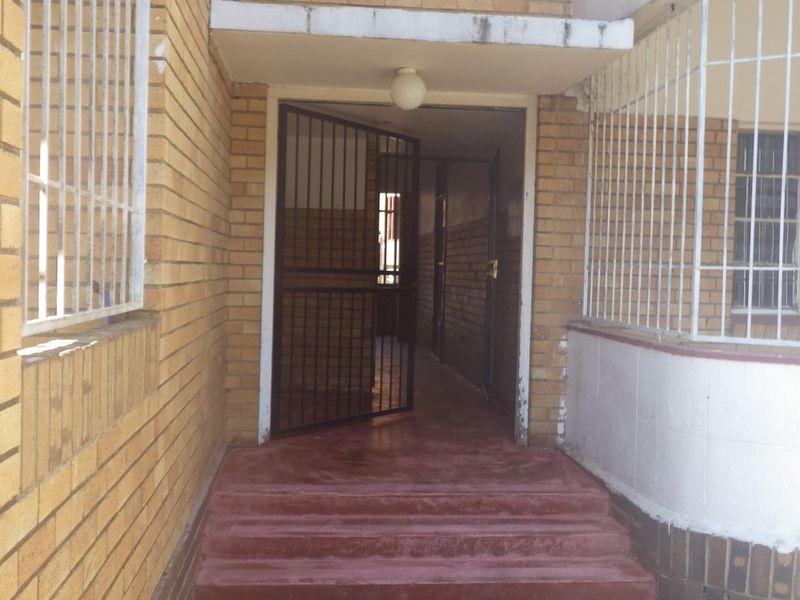 Entrance area of the flat featuring brick exterior walls, security gate, and security bars on windows with concrete steps leading to the doorway.