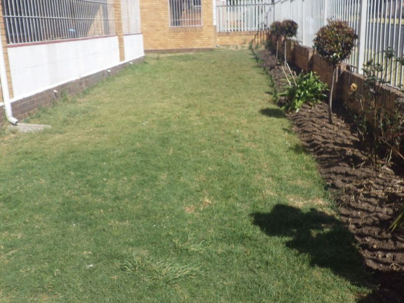 A private garden area featuring a lawn, established shrubs, and secure perimeter fencing along the brick exterior of the property.
