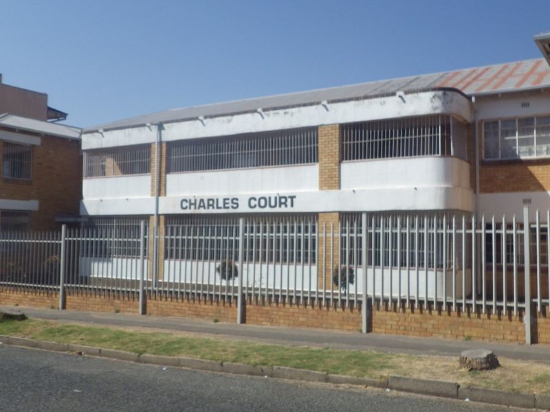 Front elevation of Charles Court, a multi-story residential flat building featuring face brick construction, security fencing, and metal roofing.