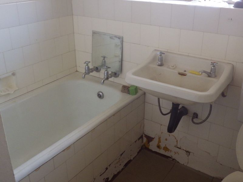A dated bathroom featuring a bathtub, wall-mounted basin, and toilet with visible wear to the wall tiles and finishes.