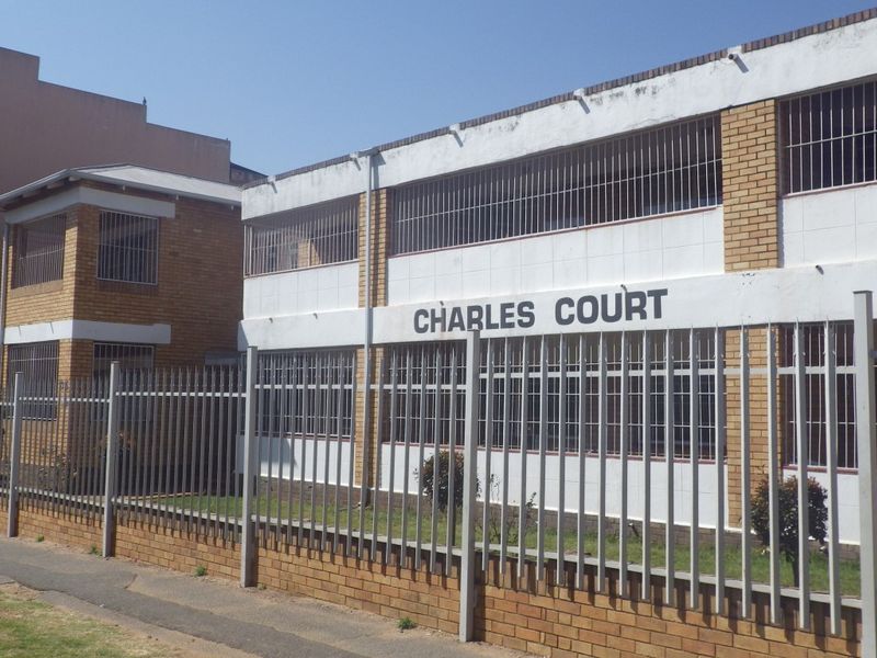 Exterior view of Charles Court apartment building featuring brick and plastered facade with security fencing and window bars.