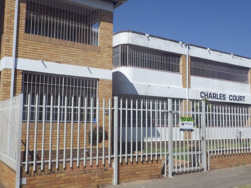 Front exterior view of Charles Court apartment building featuring brick and painted masonry facade with security fencing and bars.