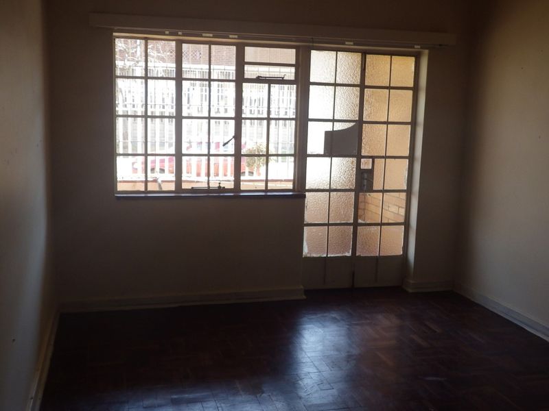 An empty living room featuring original parquet flooring and steel-framed windows and doors, requiring maintenance and cosmetic updates.