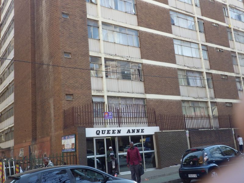 Front elevation of the Queen Anne apartment building featuring a brick facade, metal security fencing, and ground-level glass entrance.