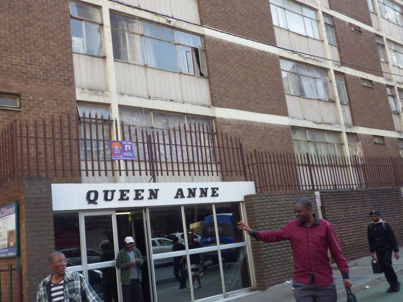 Street-level view of the Queen Anne apartment building facade, featuring brick construction, metal security fencing, and a glass-fronted entrance.