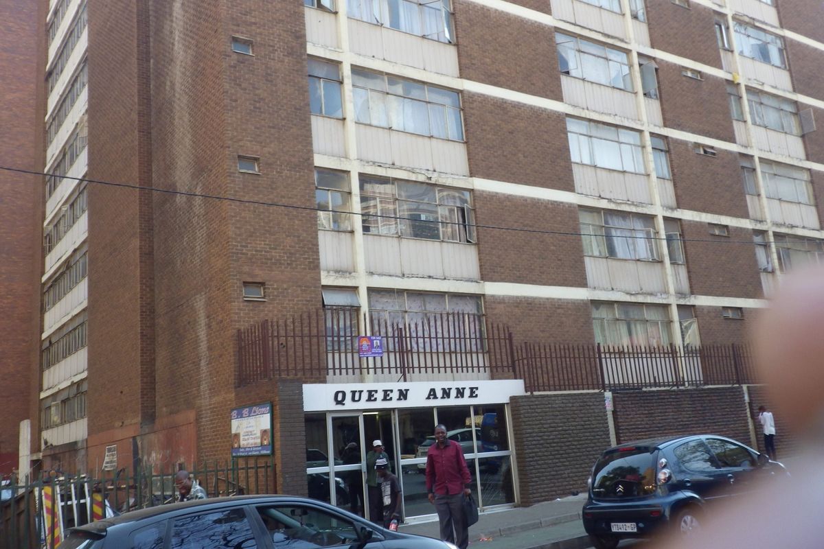 Front elevation of the Queen Anne apartment building featuring a brick facade, metal security fencing, and ground-level glass entrance.