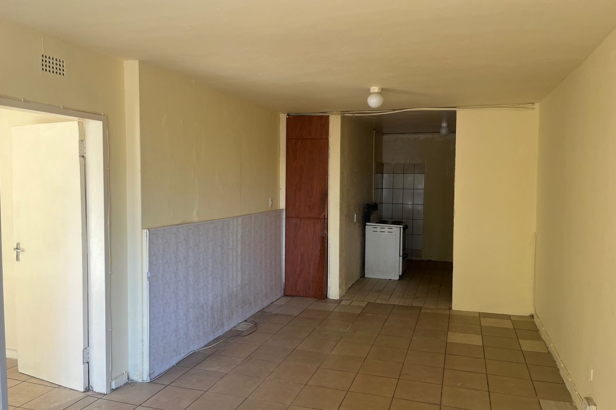 Open-plan living area featuring tiled flooring and a separate kitchen nook with a freestanding stove and tiled splashback.