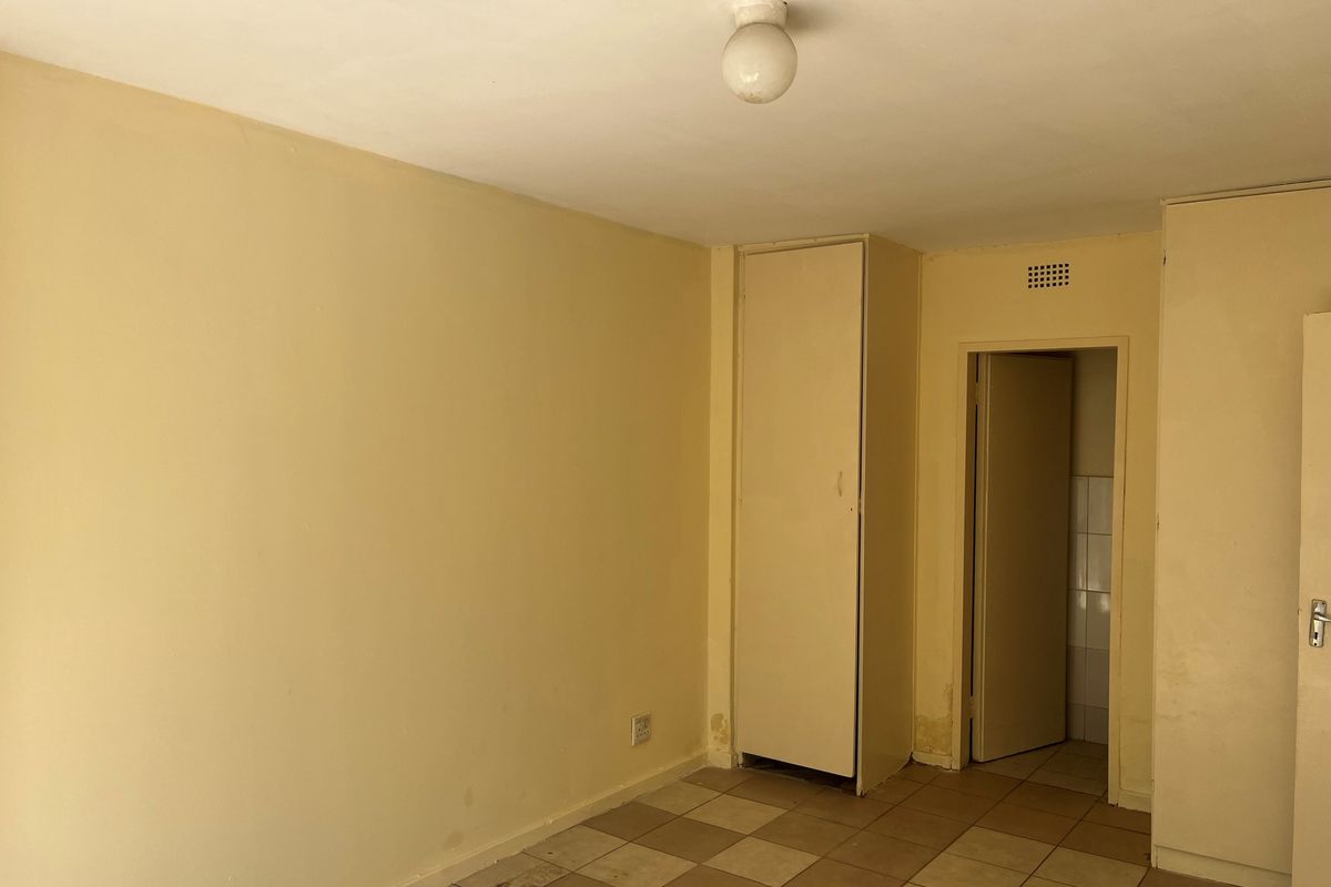 An empty bedroom featuring tiled flooring, built-in cupboards, and a neutral color palette, offering a blank canvas for renovation or interior design updates.