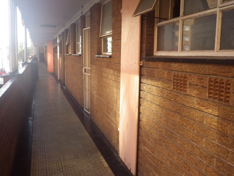 An exterior apartment building walkway featuring brick walls, tiled flooring, and security access gates to individual units.