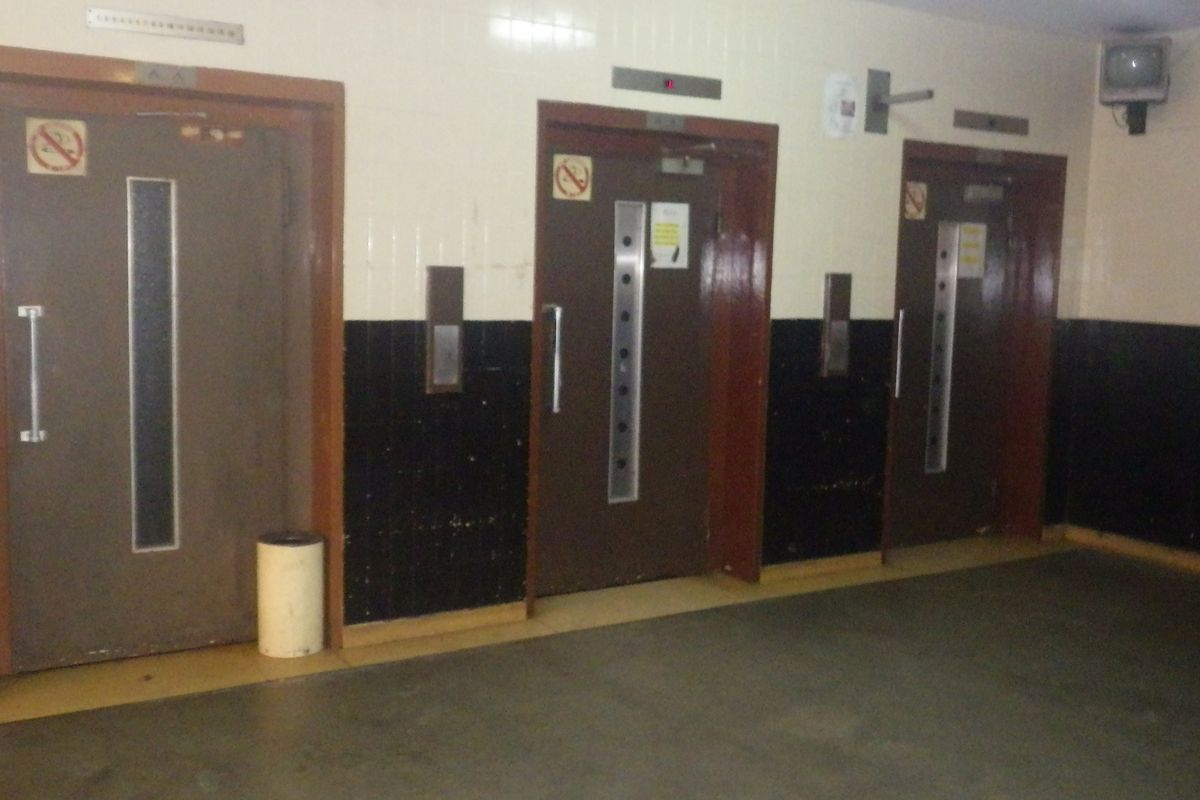 A communal hallway area featuring three elevator access points with dated wall tiling and flooring.